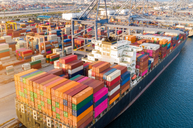 Large cargo ship docked at a busy port, loaded with colorful shipping containers, representing global trade and logistics.
