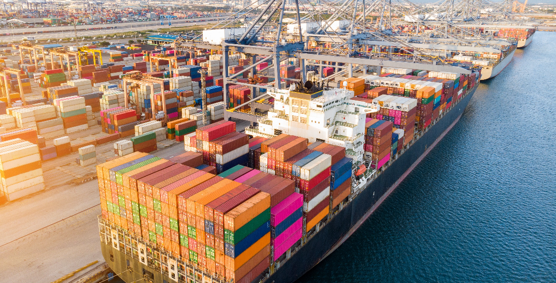 Large cargo ship docked at a busy port, loaded with colorful shipping containers, representing global trade and logistics.