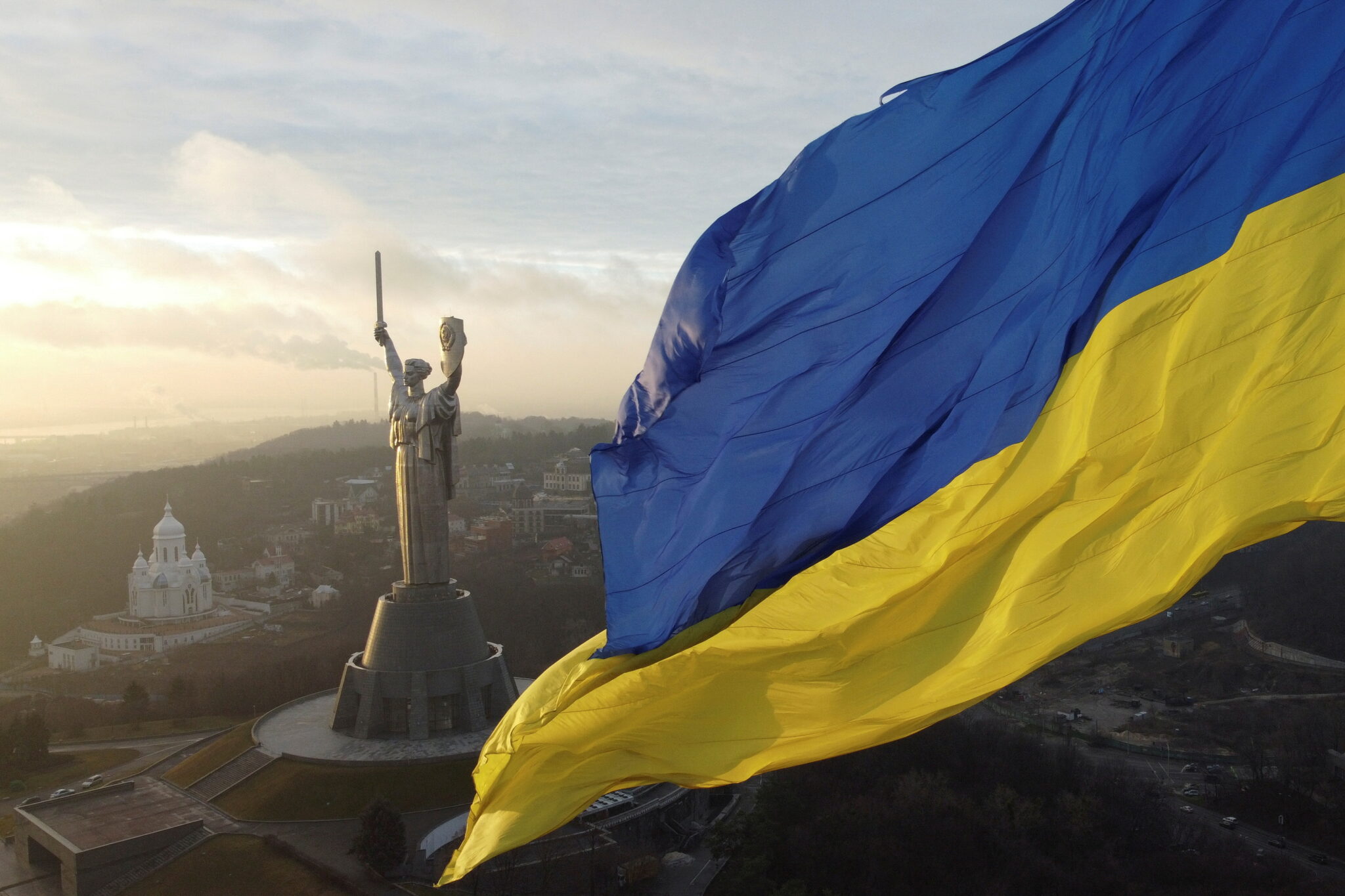 Ukrainian flag waving in front of the Motherland Monument in Kyiv at sunrise, symbolizing national resilience and unity during the Russian-Ukrainian war.