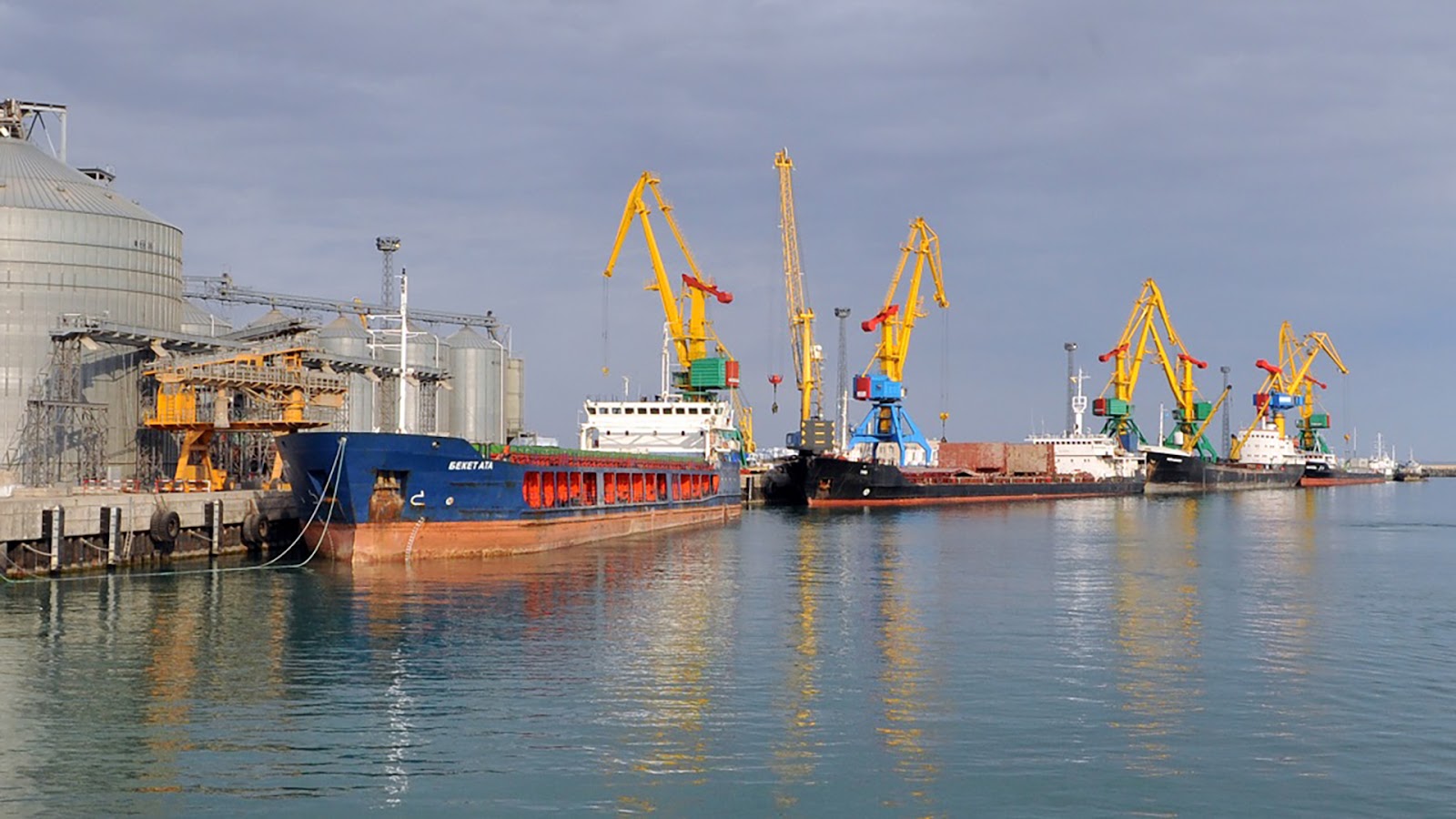 A port terminal in Kazakhstan with cargo ships and large cranes facilitating oil exports via the Caspian Sea. The infrastructure highlights Kazakhstan’s alternative oil export routes.