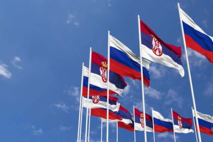 Multiple Serbian and Russian flags waving against a blue sky, symbolizing diplomatic relations and political ties between Serbia and Russia.